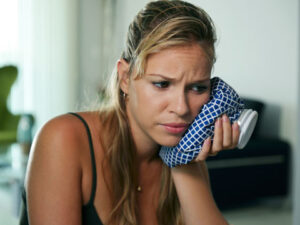 Young woman with toothache holding ice bag on cheek
